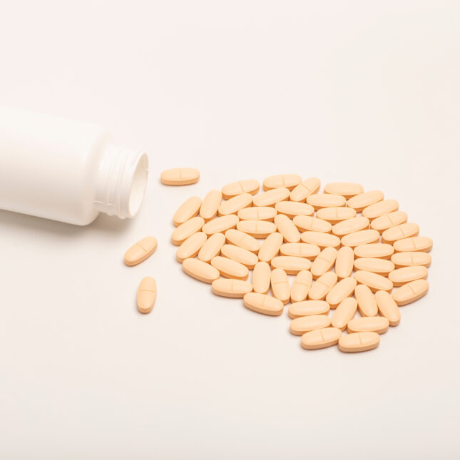 Photo of a prescription bottle tipped over with peach color pills in the shape of a brain beside it. -- first opinion coverage from STAT