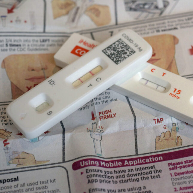 Two positive covid tests are stacked diagonally on each other on a manual — health coverage from STAT