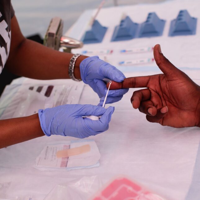 A medical staff holds a person's index finger, extracting blood for an HIV test — health coverage from STAT