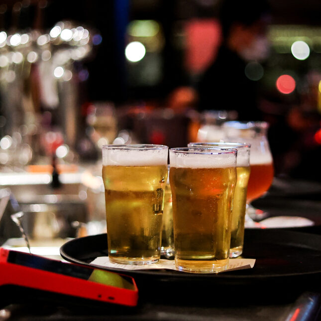 Four full cups of beers on a tray, sitting on a bar counter under dim light — health coverage from STAT