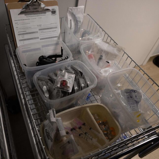 A cart hosts medical equipment at a supervised drug injection site. The items include forms on clipboards, Narcan nasal sprays, oral airways, syringes — first opinion coverage from STAT