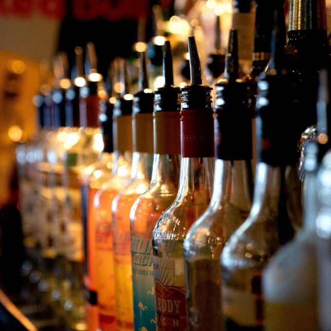 Dozens of different alcohol bottles line up on a bar counter — health coverage from STAT