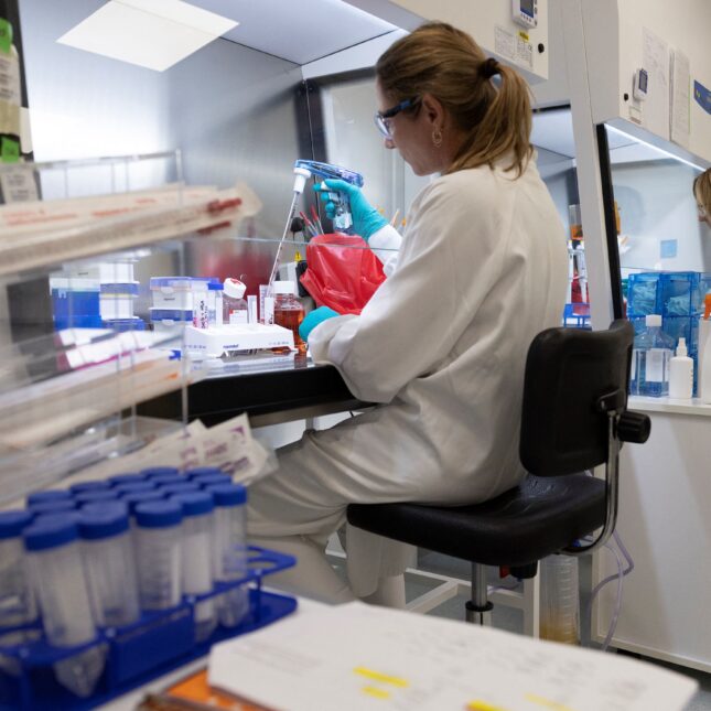 Two researchers in white coats sat in separate stations next to each other, operating lab equipment in an oncology laboratory of French pharmaceutical company Sanofi — first opinion coverage from STAT