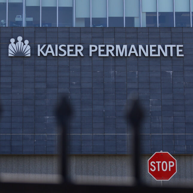 A stop sign stands in between a Kaiser Permanente building and a gate — health tech coverage from STAT