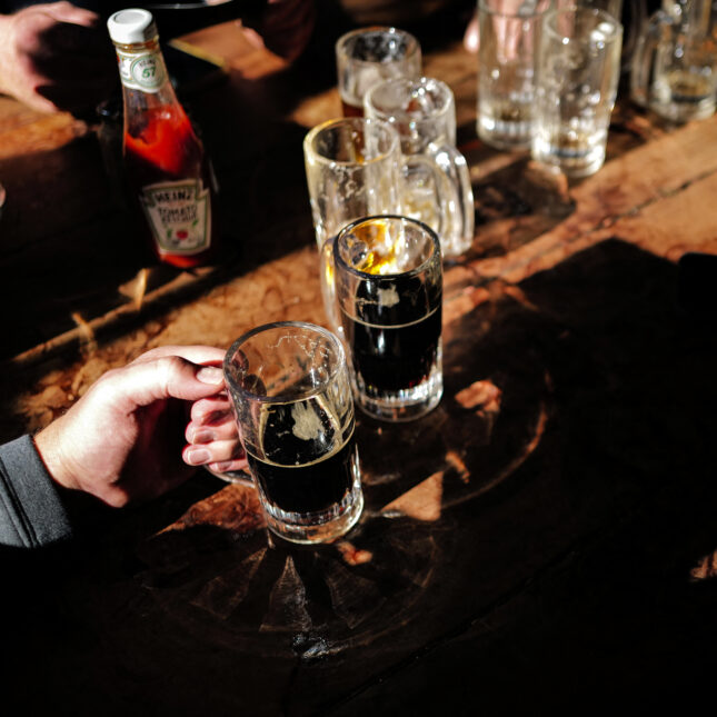 Photograph of people drinking beer at a bar in New York City. Close up on hands holding glasses of beer.