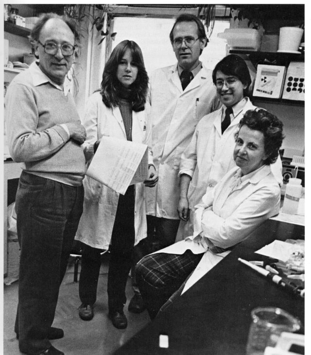 Black and white archival photograph of Dr. Ruth Nussenzweig (far right), Dr. Victor Nussenzweig (far left) and their team at NYU Drs. Joan Ellis, Alan H. Cochrane, and Fidel Zavala (left to right), pictured in one of NYU's parasitology labs