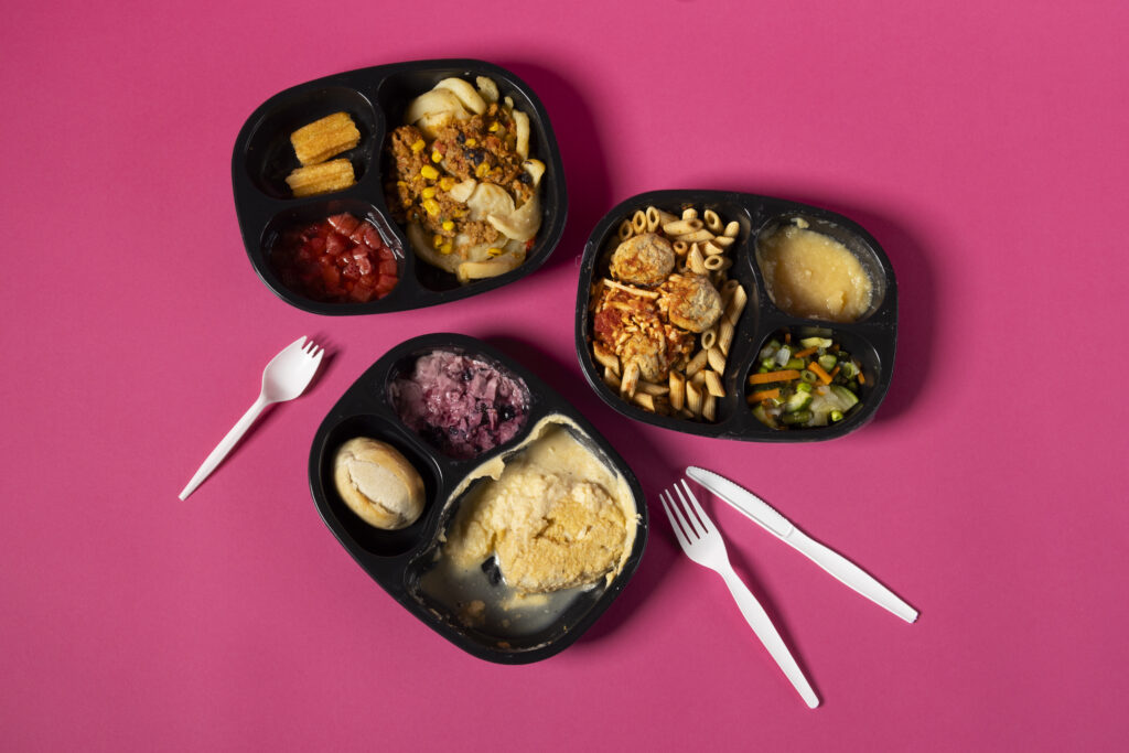 A selection of Homestyle Direct entrees photographed on a bright fuschia backdrop with plastic cutlery